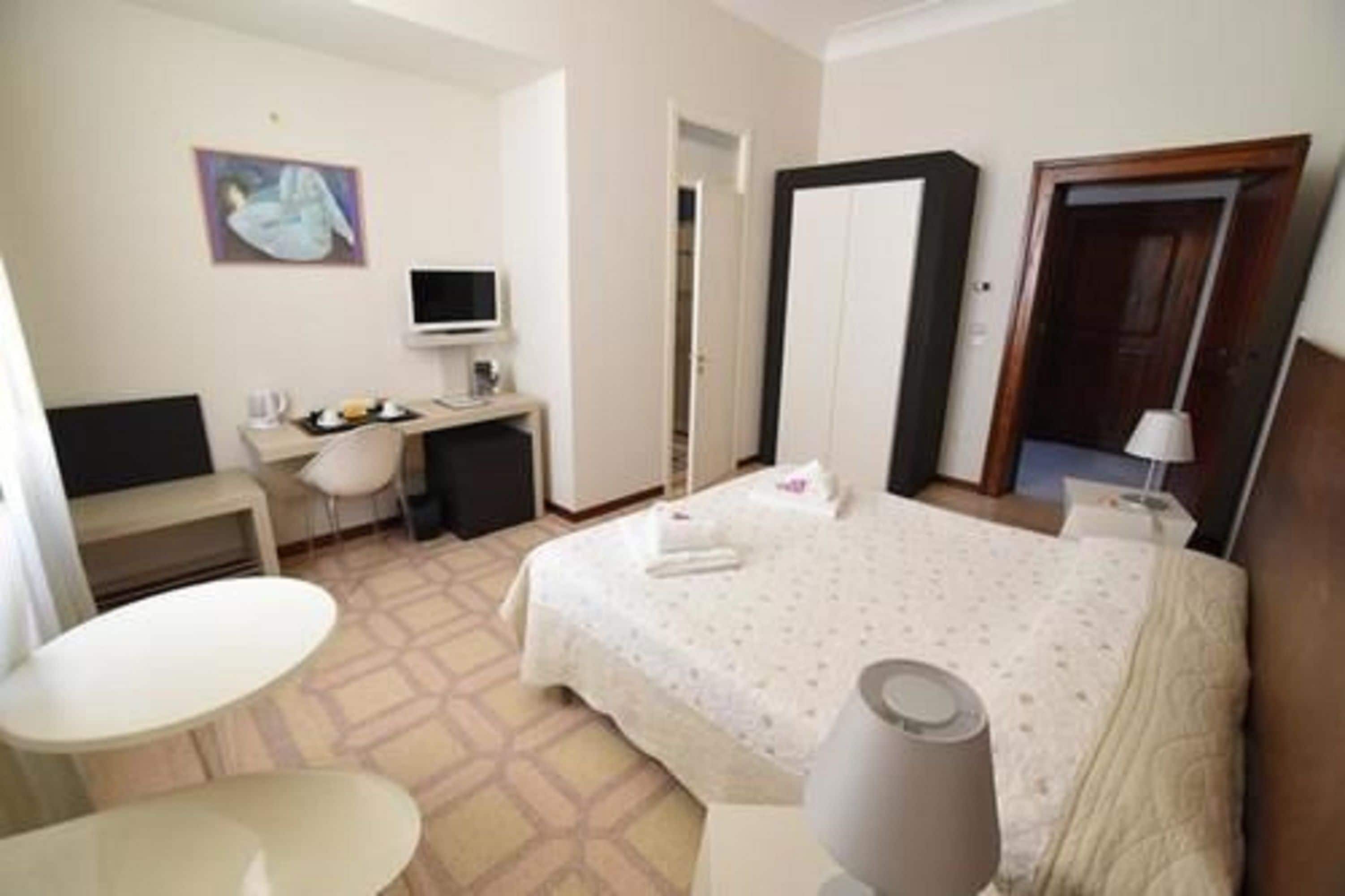A hotel room with a bed, a desk, a chair, a television, and a painting on the wall.