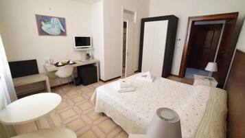 A hotel room with a bed, a desk, a chair, a television, and a painting on the wall.