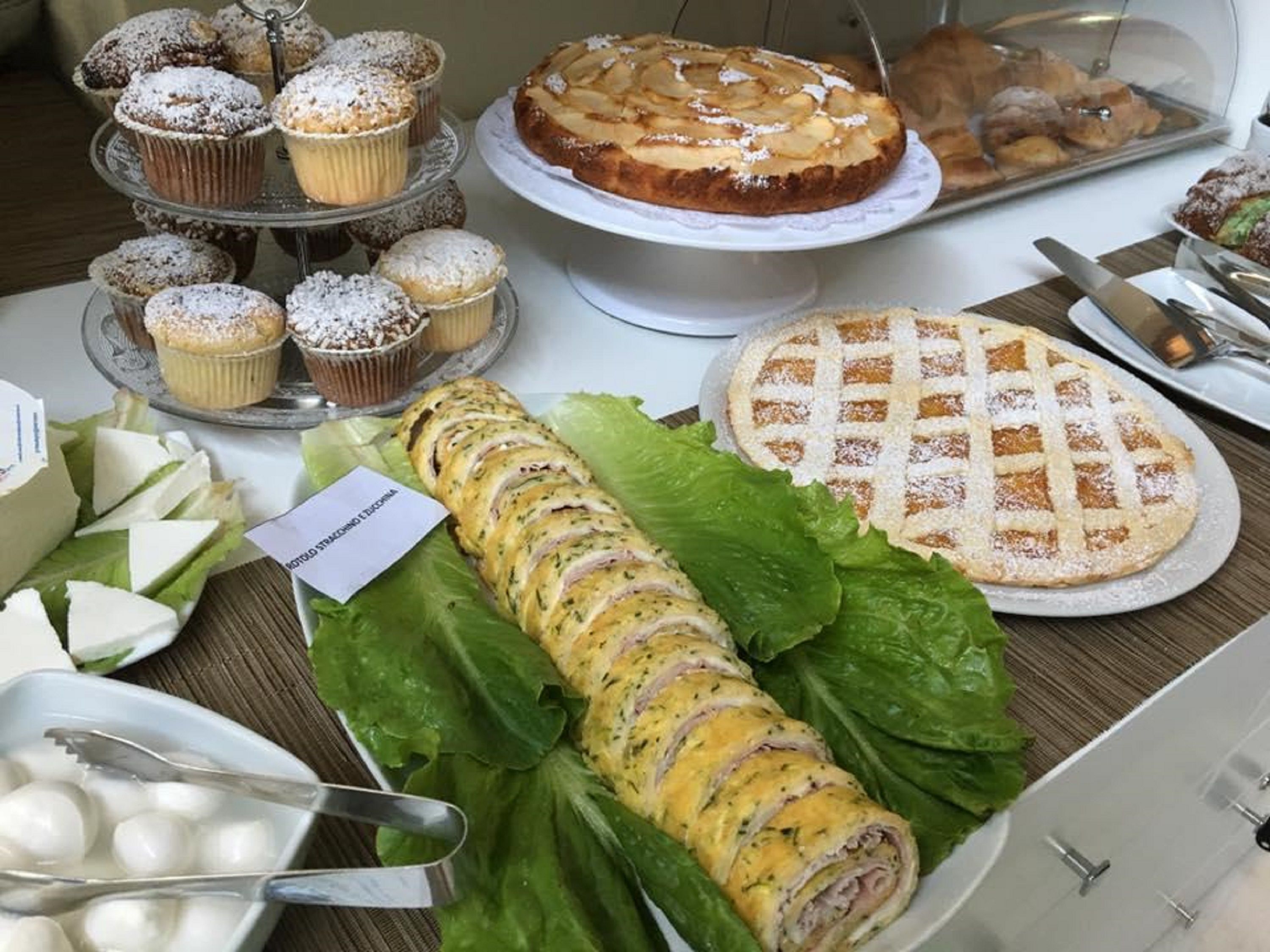 A buffet table with various food items including pastries, a rolled omelette, and a lattice-topped pie.