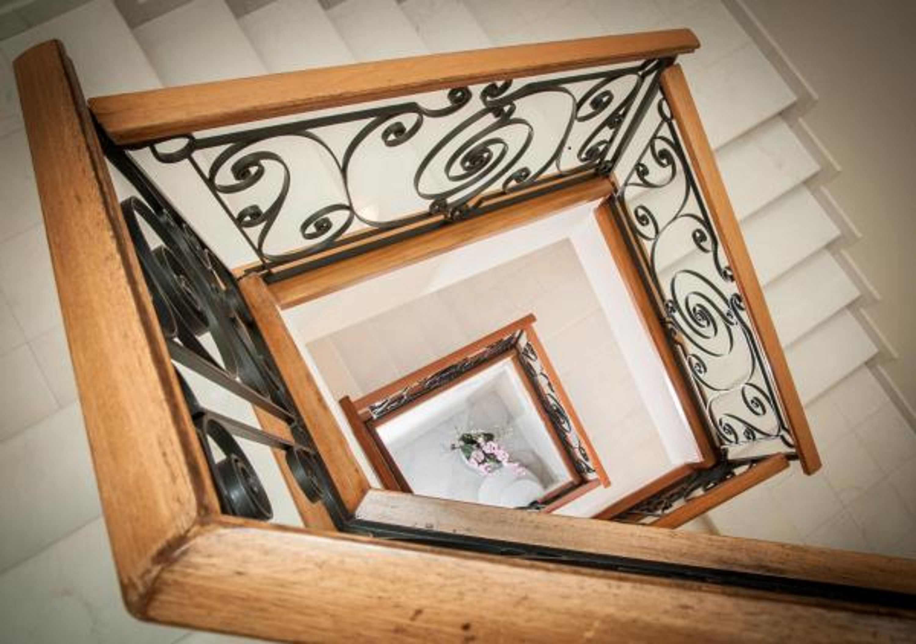 A wooden staircase with ornate black metal railings and a framed picture at the top.