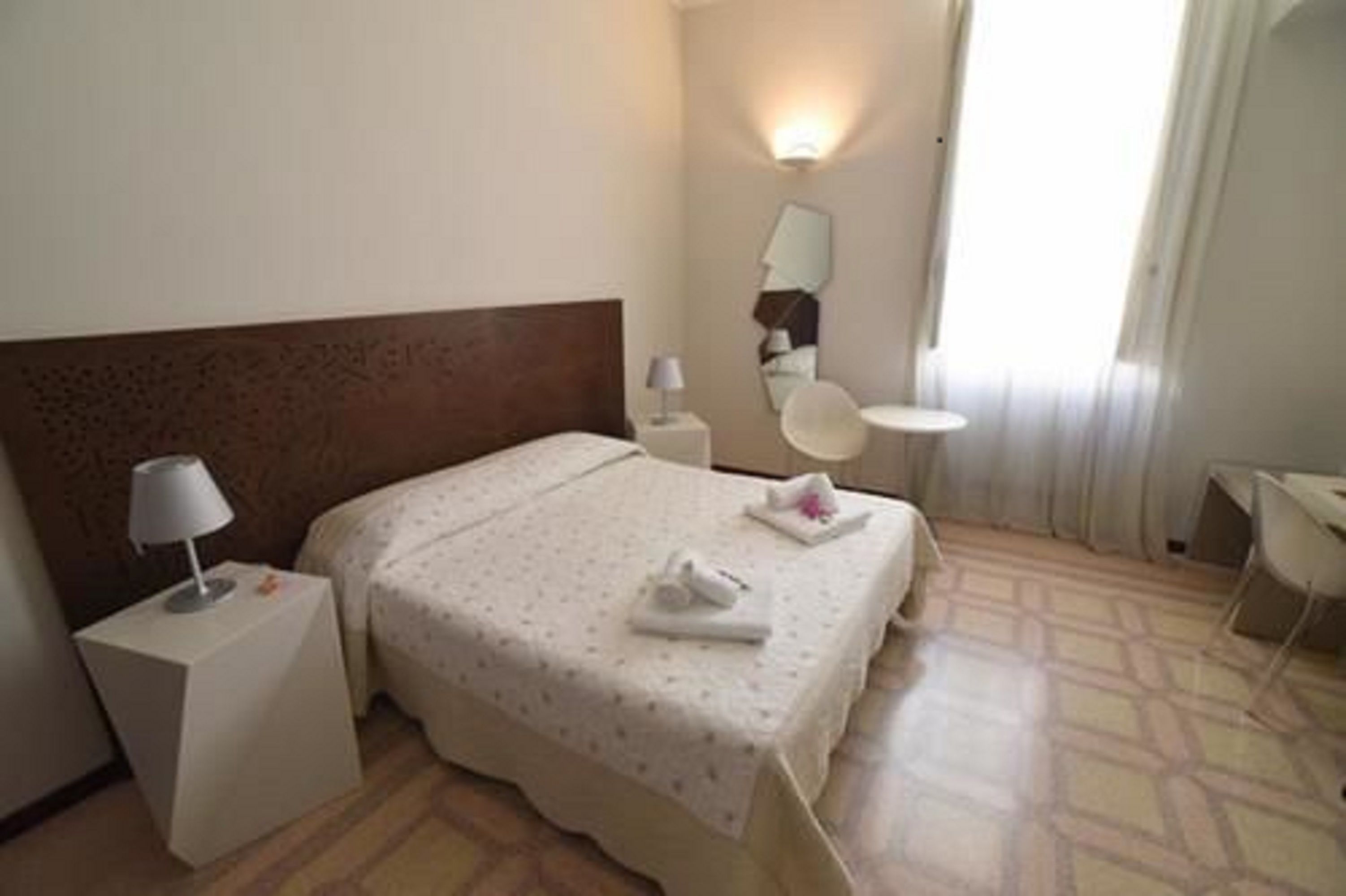 Habitación de hotel con cama, mesita de noche con lámpara, una mesita redonda y una silla.