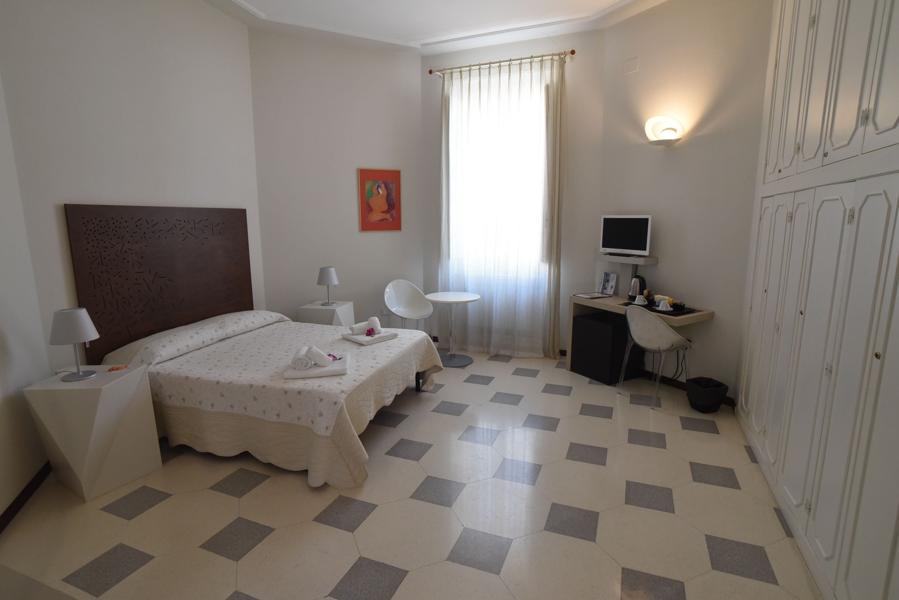 A hotel room with a bed, two bedside tables, a desk with a chair, a television, and a wardrobe.