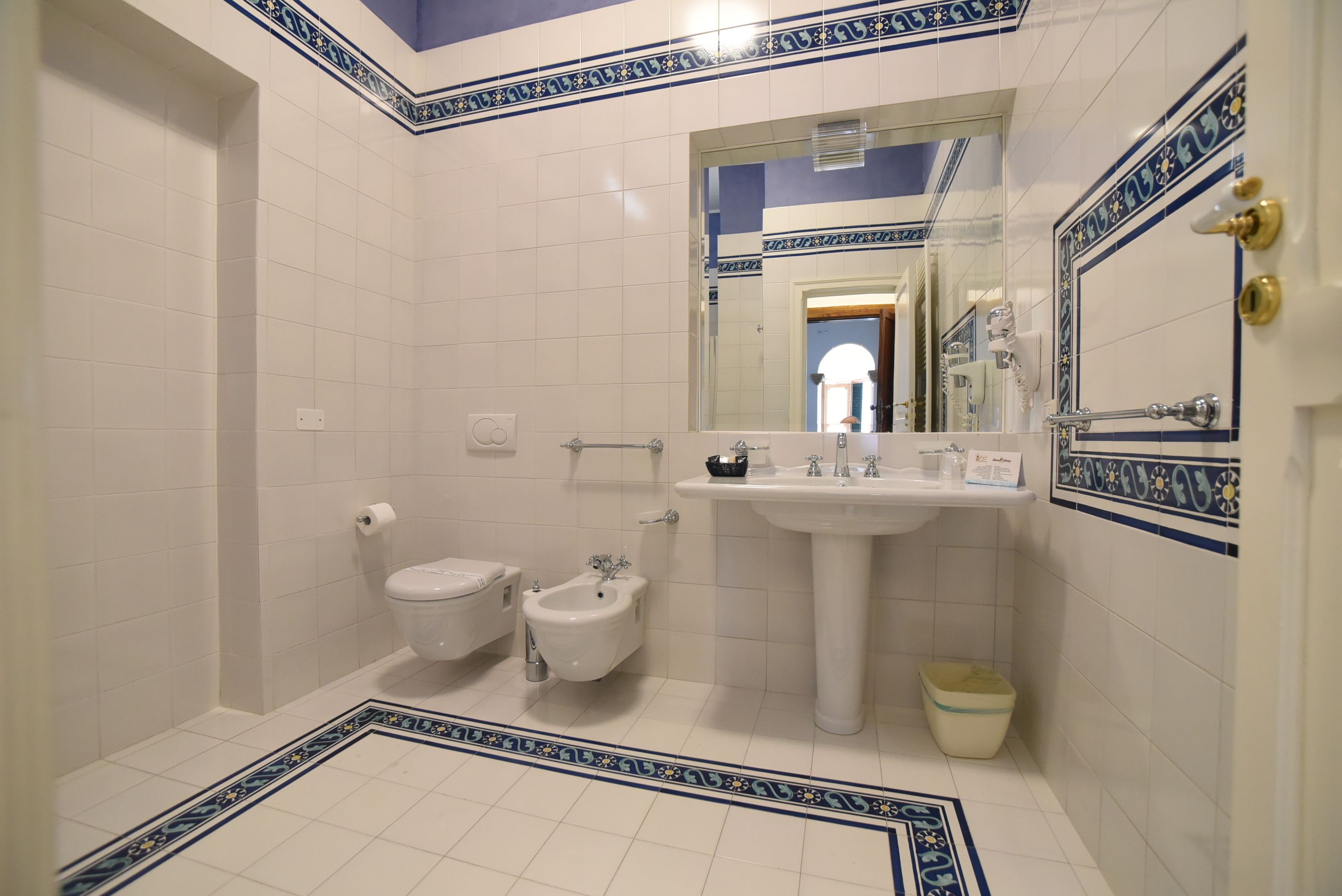 Un baño con inodoro, bidé, lavamanos y espejo.