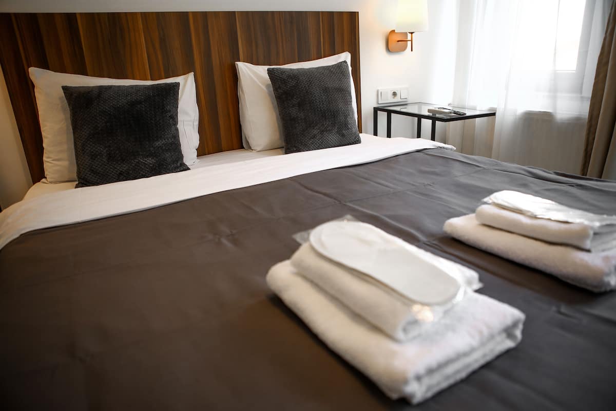 A hotel room with a large bed, two pillows, a bedside table with a lamp, and towels on the bed.