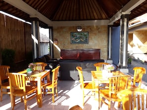 A covered outdoor seating area with wooden furniture and a stone wall. - Villa Amari (Penida Island)
