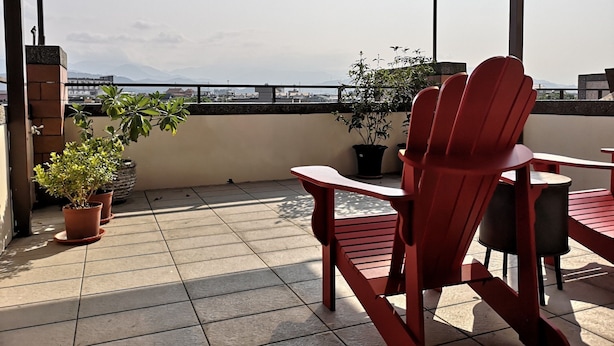 A red chair and table on a balcony with potted plants and a view of the cityscape. - Chance Encounter (Luodong)