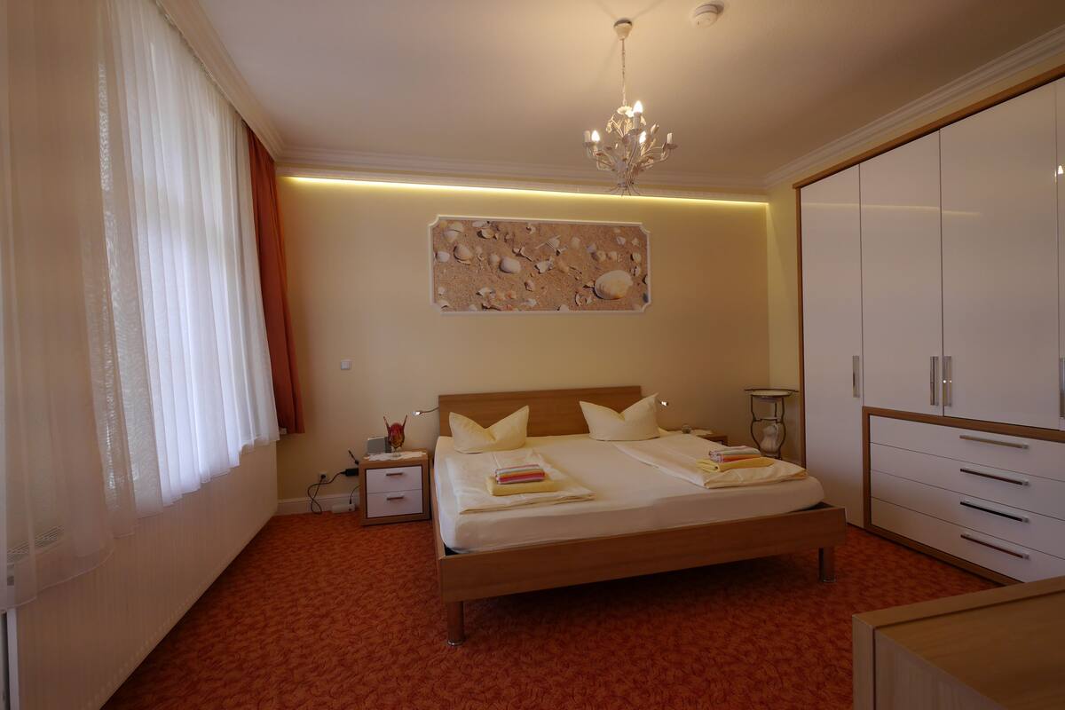 A bedroom with a bed, bedside table, lamp, wardrobe, and a wall with a seashell artwork.