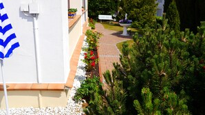 Un sendero lleva a un edificio de fachada blanca y un jardín con plantas en macetas y una fuente para pájaros.
