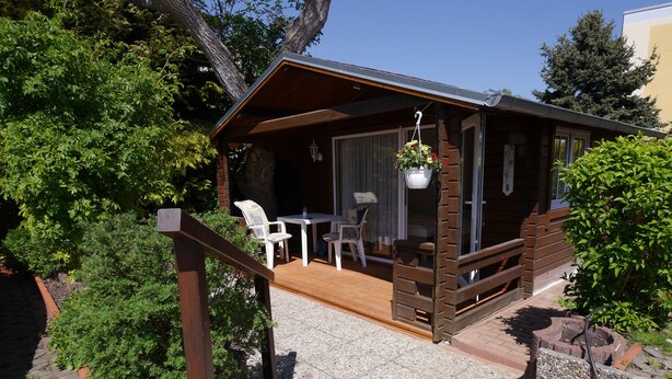 Una cabaña de madera con un patio amueblado, que incluye una mesa y sillas, rodeada de follaje.