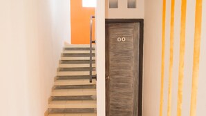 A staircase leading to a door with a simple design, a tiled floor, and a plain wall with a vertical stripe pattern. - Adikara Renon (Denpasar)
