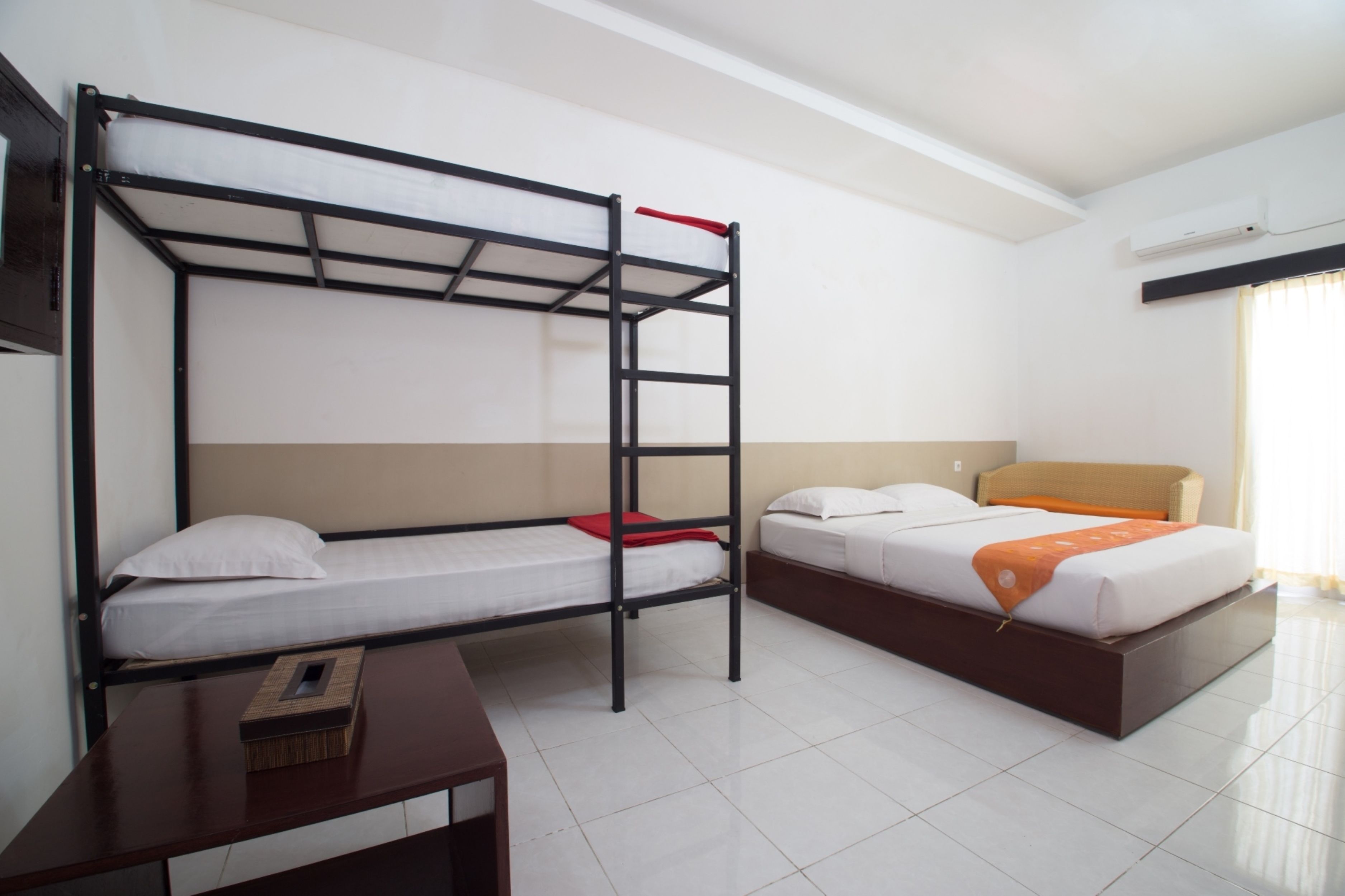 A hotel room with a bunk bed, a single bed, a wooden nightstand, and a window with curtains.