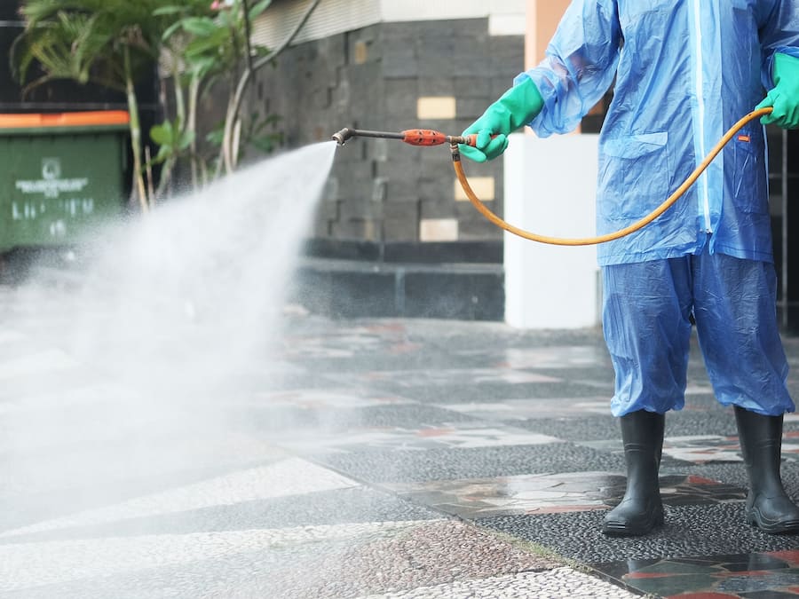 Une personne portant un équipement de protection et utilisant un tuyau pour pulvériser de l’eau.