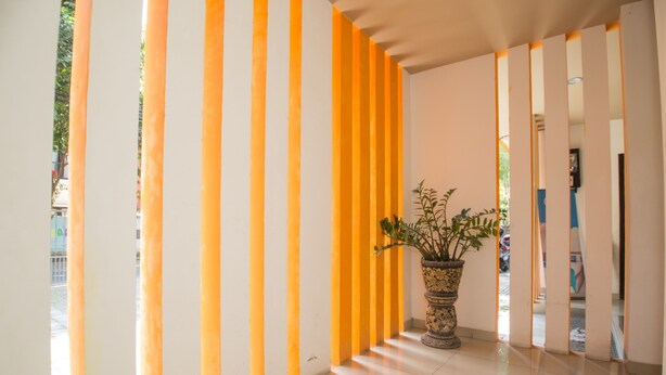 A hallway with alternating white and yellow vertical panels, a potted plant, and a tiled floor. - Adikara Renon (Denpasar)