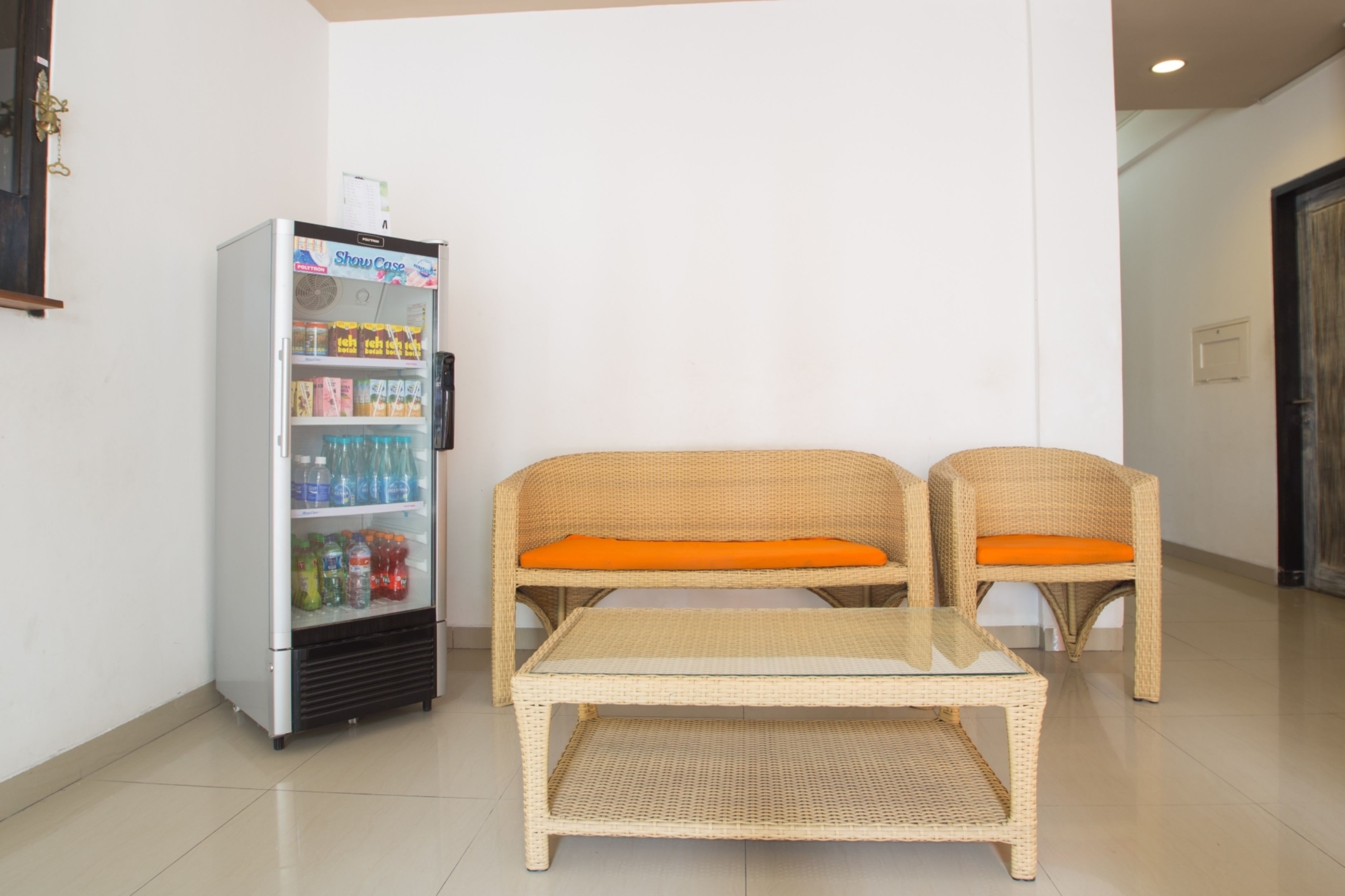 Una habitación con una máquina expendedora, dos sofás de mimbre con cojines naranja y una mesa con cubierta de vidrio.