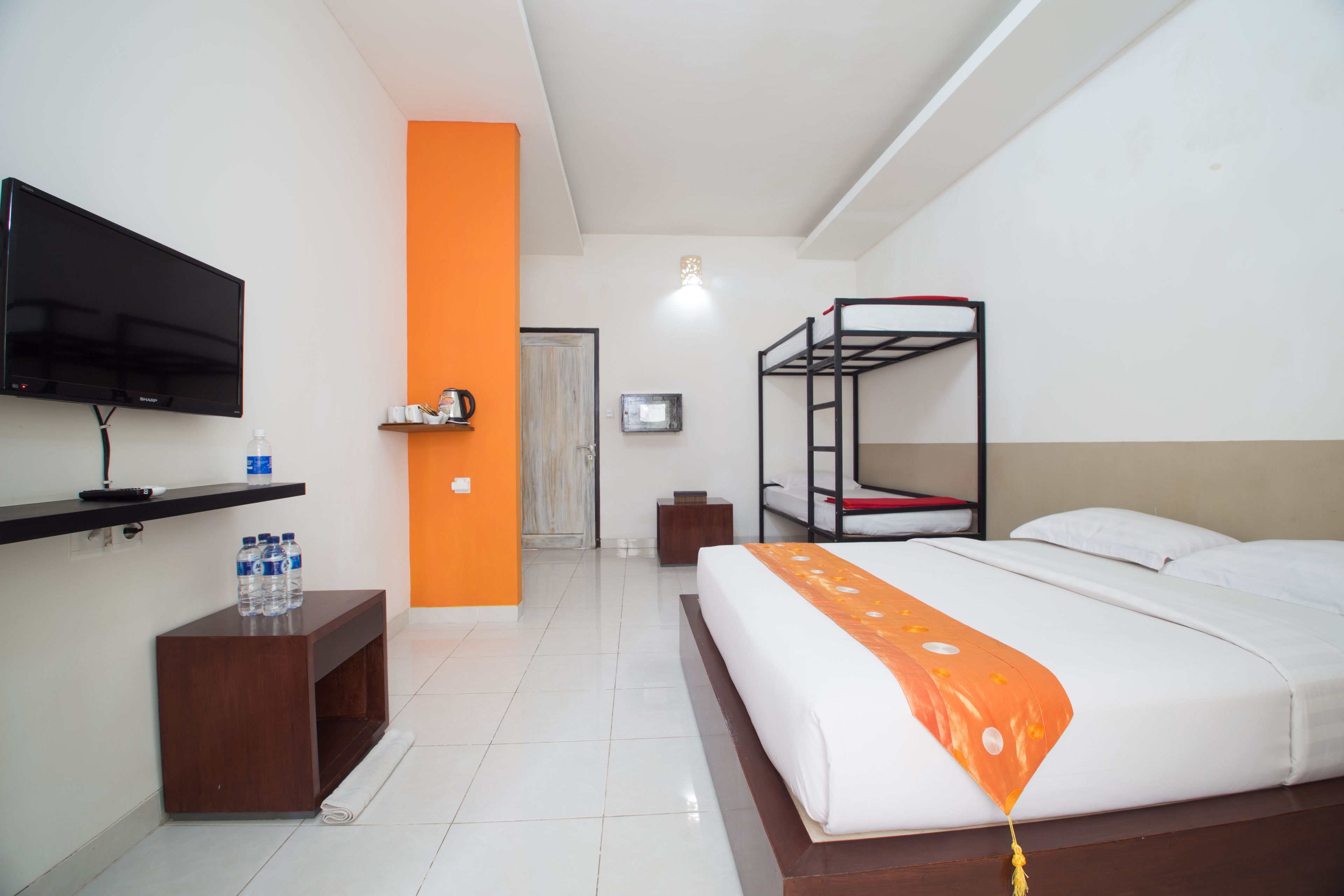 Habitación de hotel con literas, un televisor de pantalla plana, una mesita de madera con botellas de agua y una pared de acento naranja brillante.