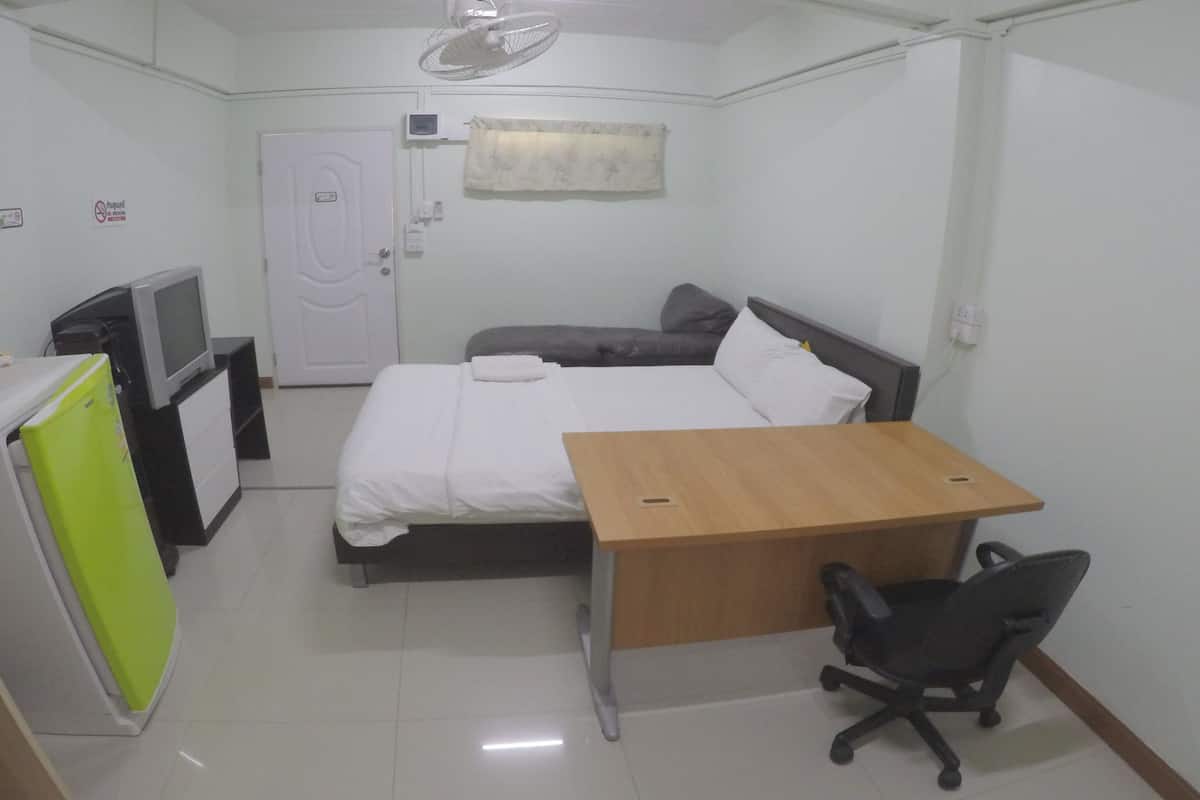 A compact hotel room with a bed, a desk, a chair, a television, and a refrigerator.