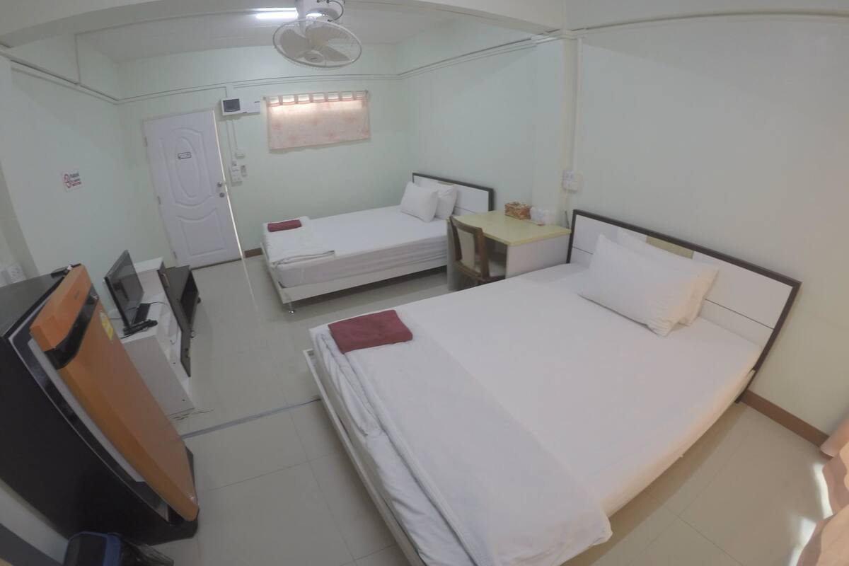 A hotel room with two beds, a desk, a chair, a wardrobe, and a ceiling fan.