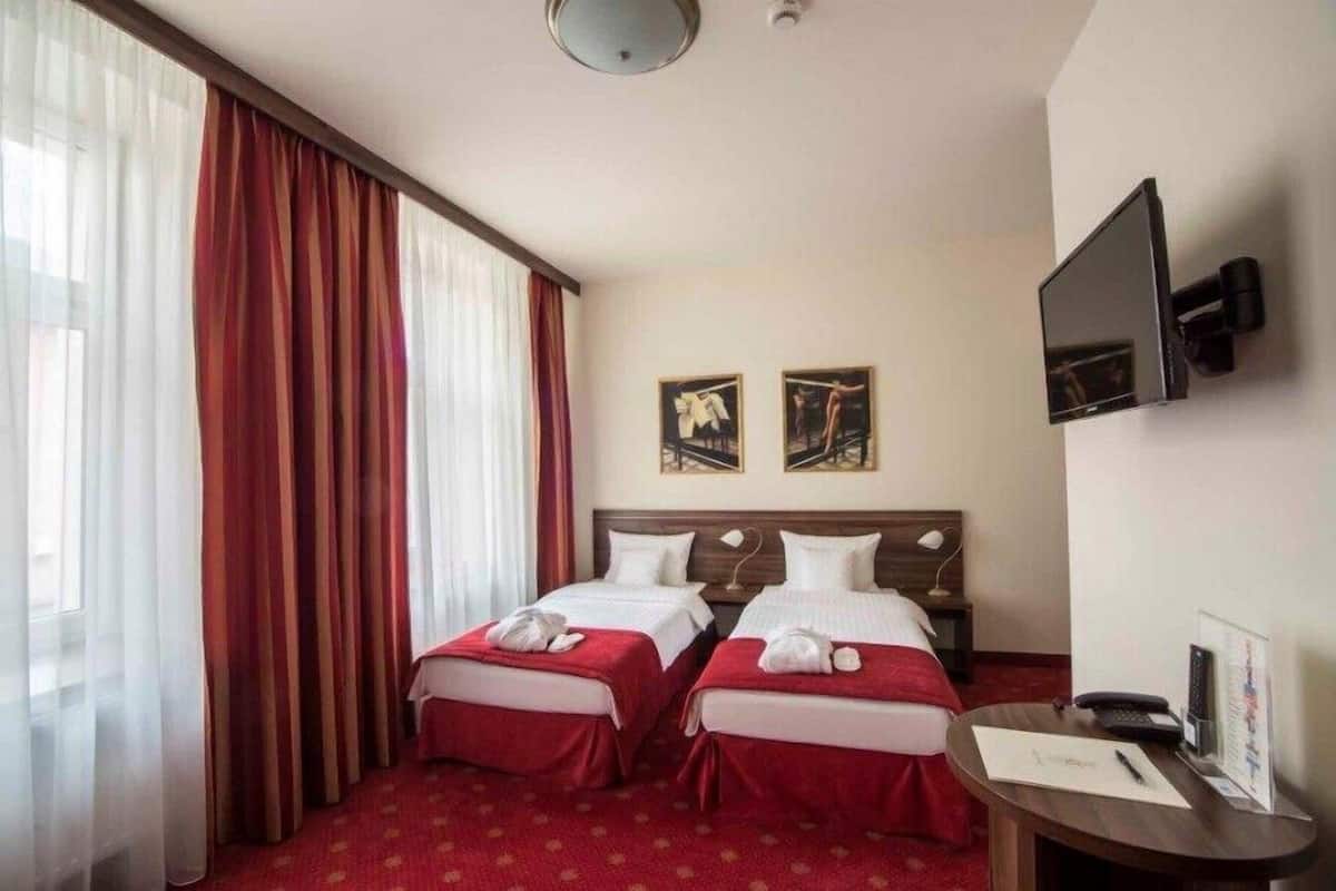 A hotel room with two beds, a desk with a computer, and a TV mounted on the wall.