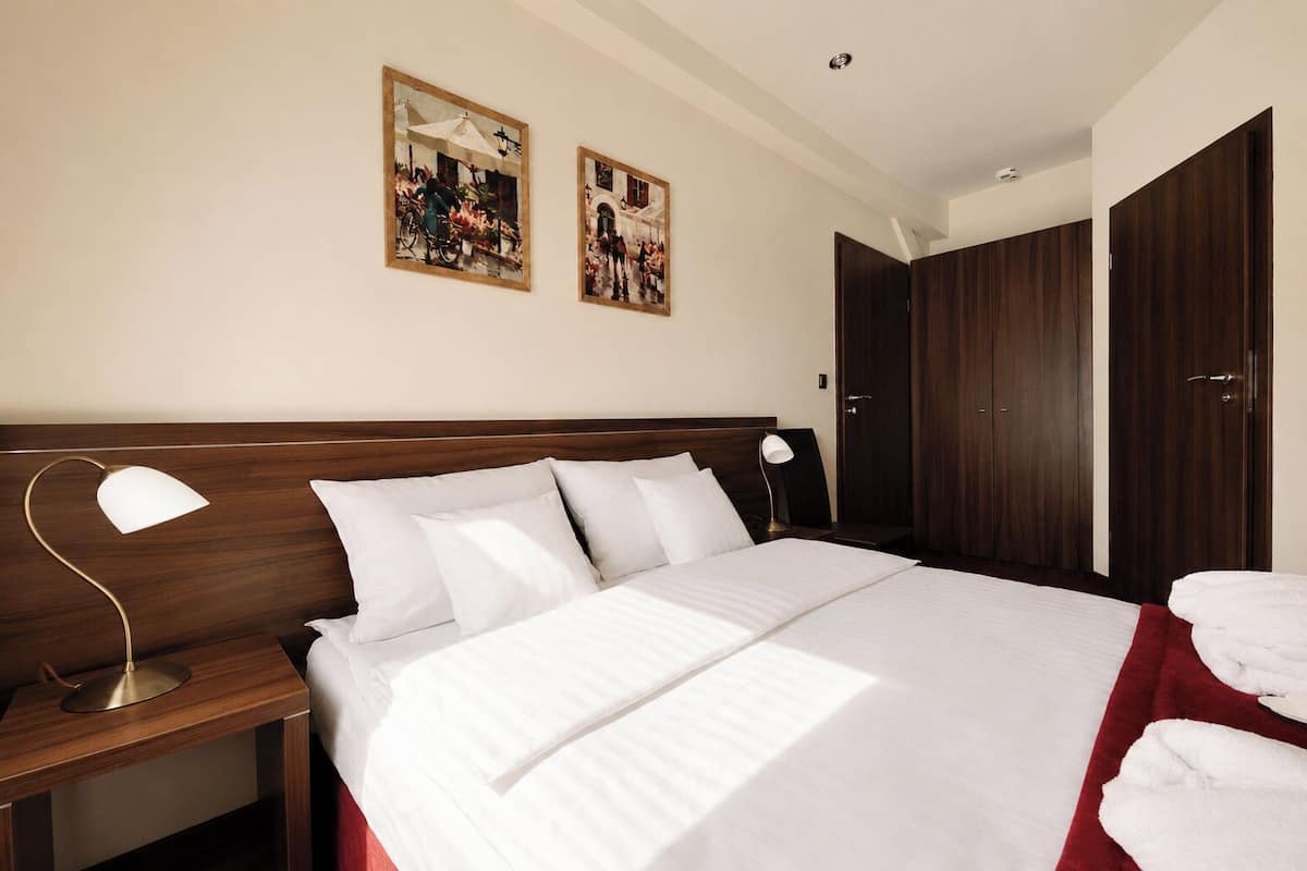 A hotel room with a large bed, two bedside lamps, a wooden headboard, and two framed pictures on the wall.