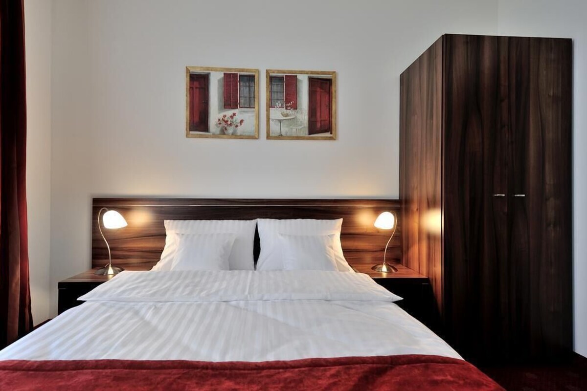 A neatly made bed with white linens, two bedside lamps, and a large wardrobe.