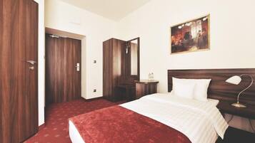 A hotel room with a large bed, a wooden wardrobe, a bedside table with a lamp, and a painting on the wall.