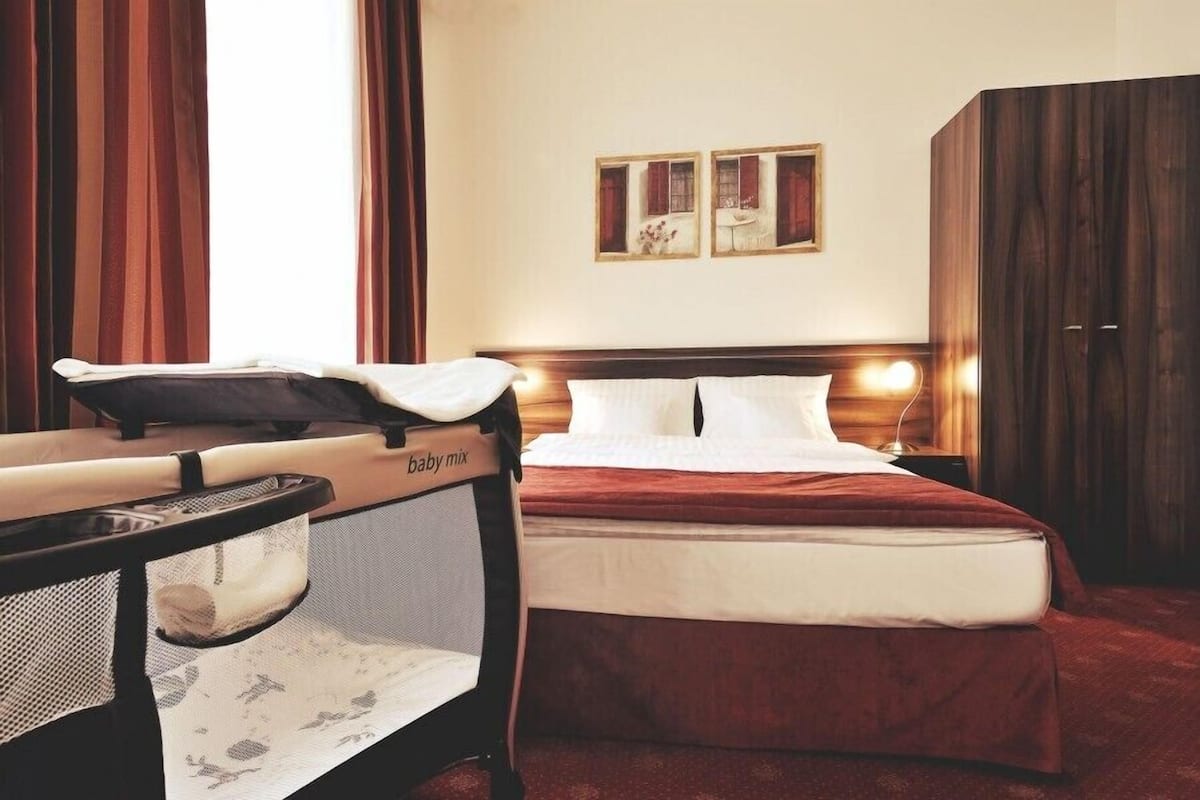 A hotel room with a bed, a small table with a baby changing station, a wardrobe, and two framed pictures on the wall.