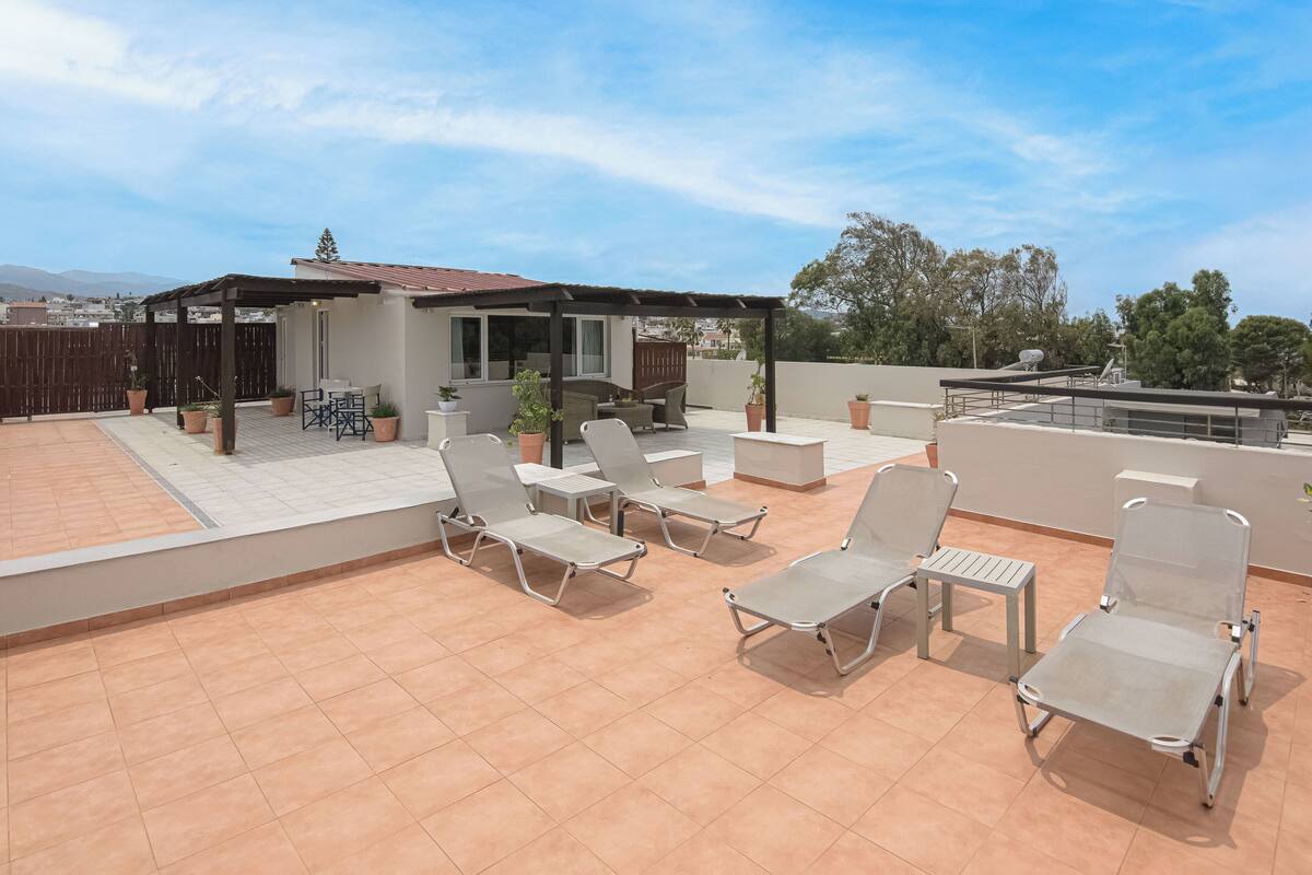 A rooftop patio with four lounge chairs, a small table, and a covered seating area.