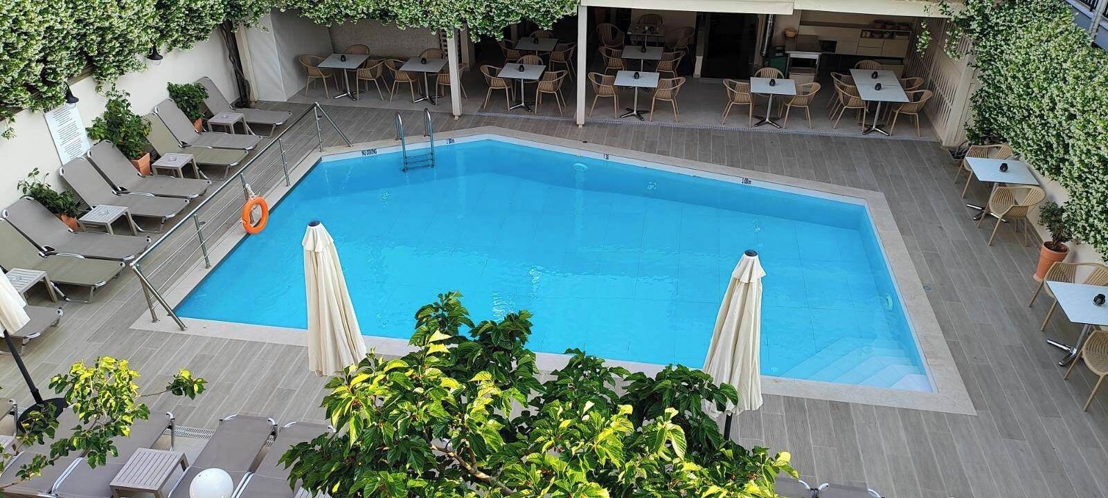 A rectangular pool with a lifeguard chair and a lifebuoy, surrounded by lounge chairs and tables.