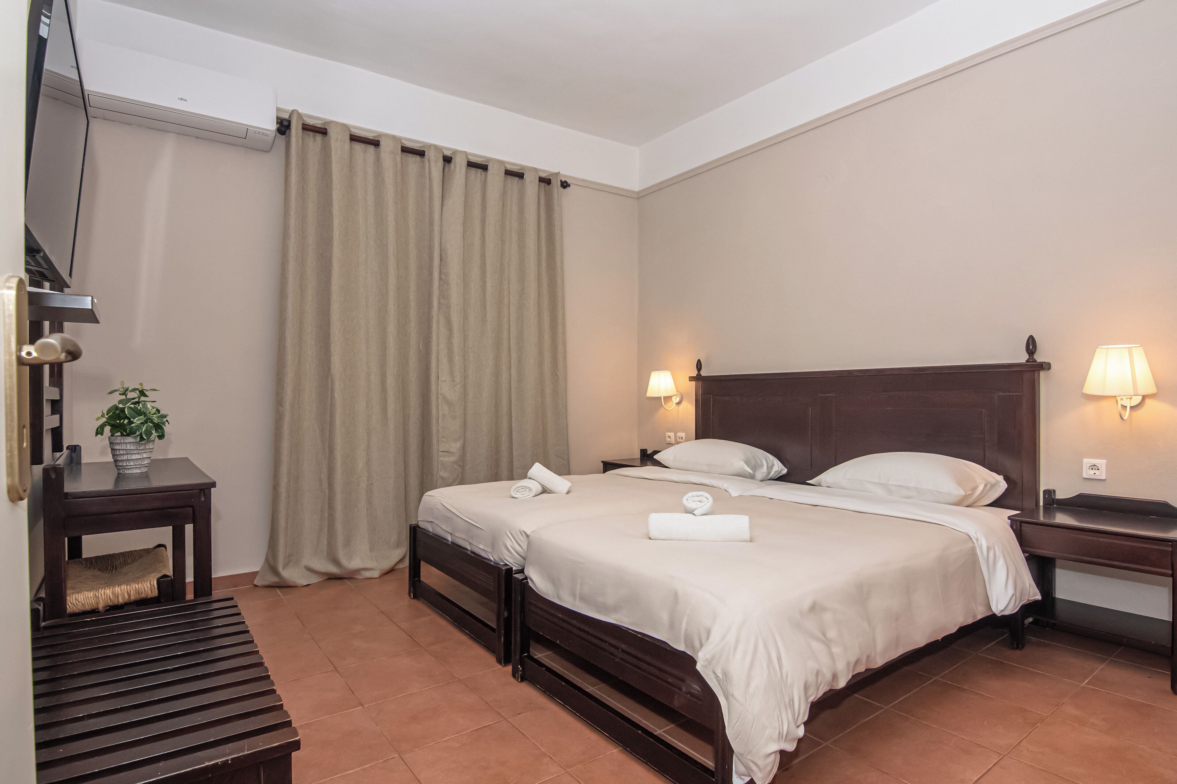 A hotel room with a bed, bedside tables, a TV, and a curtain.