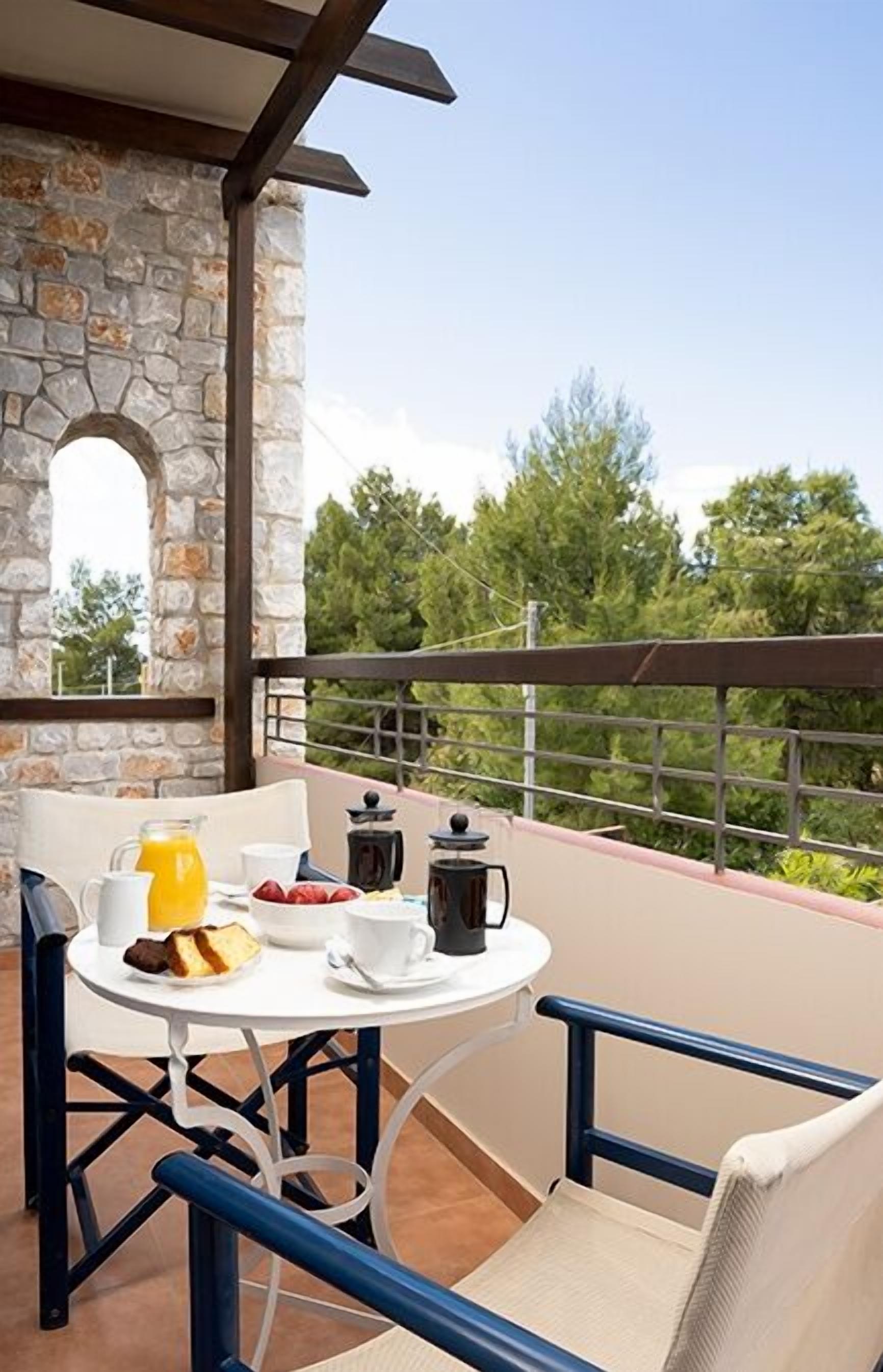 A balcony with a stone wall, a table with breakfast items, and a view of trees.
