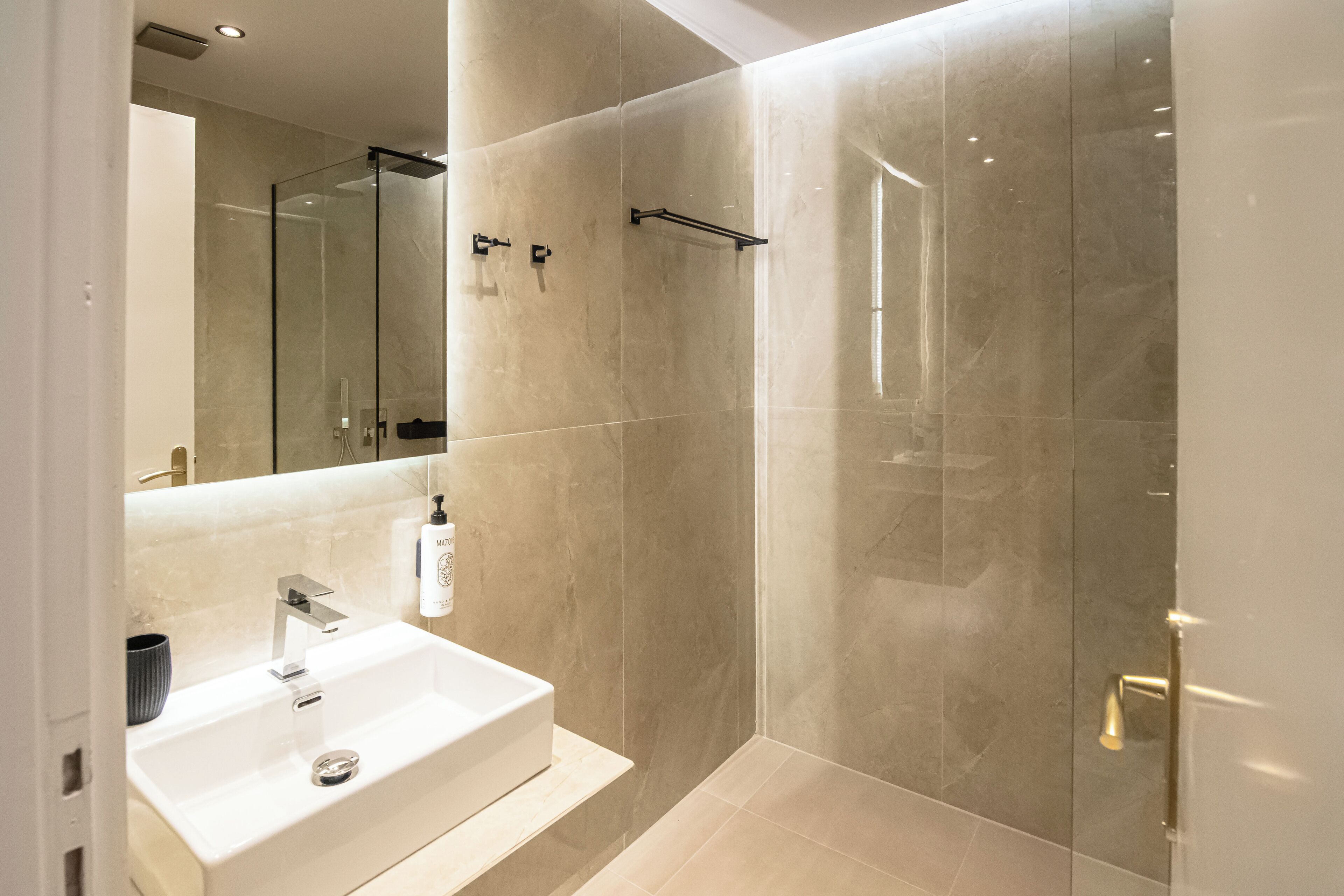 A modern bathroom with a white sink, a glass shower enclosure, and a large mirror.
