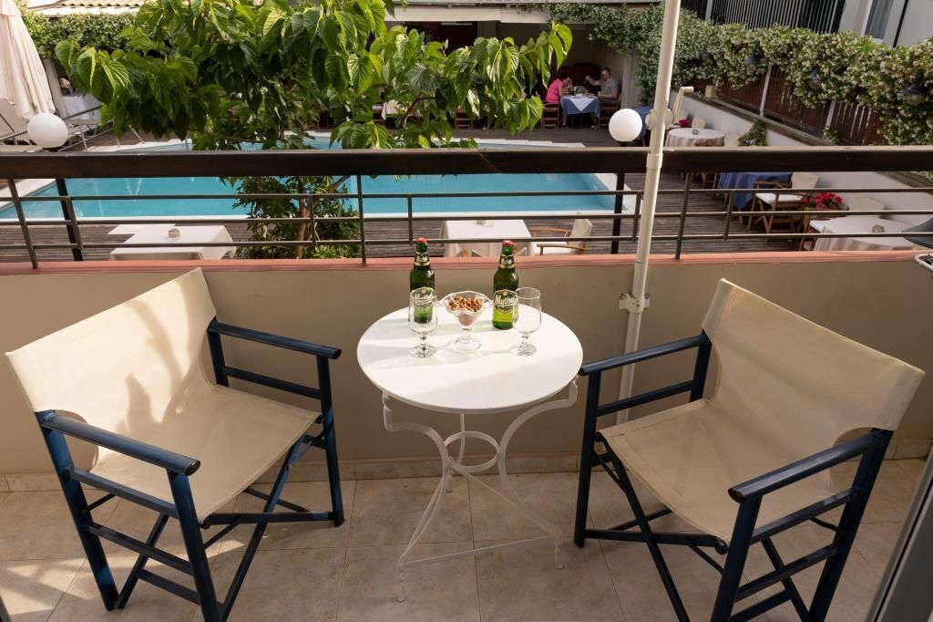 A balcony with two chairs and a table, overlooking a pool and a dining area.