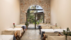 Un restaurant amb parets de pedra, taules amb estovalls blancs i una vista per una porta de vidre.