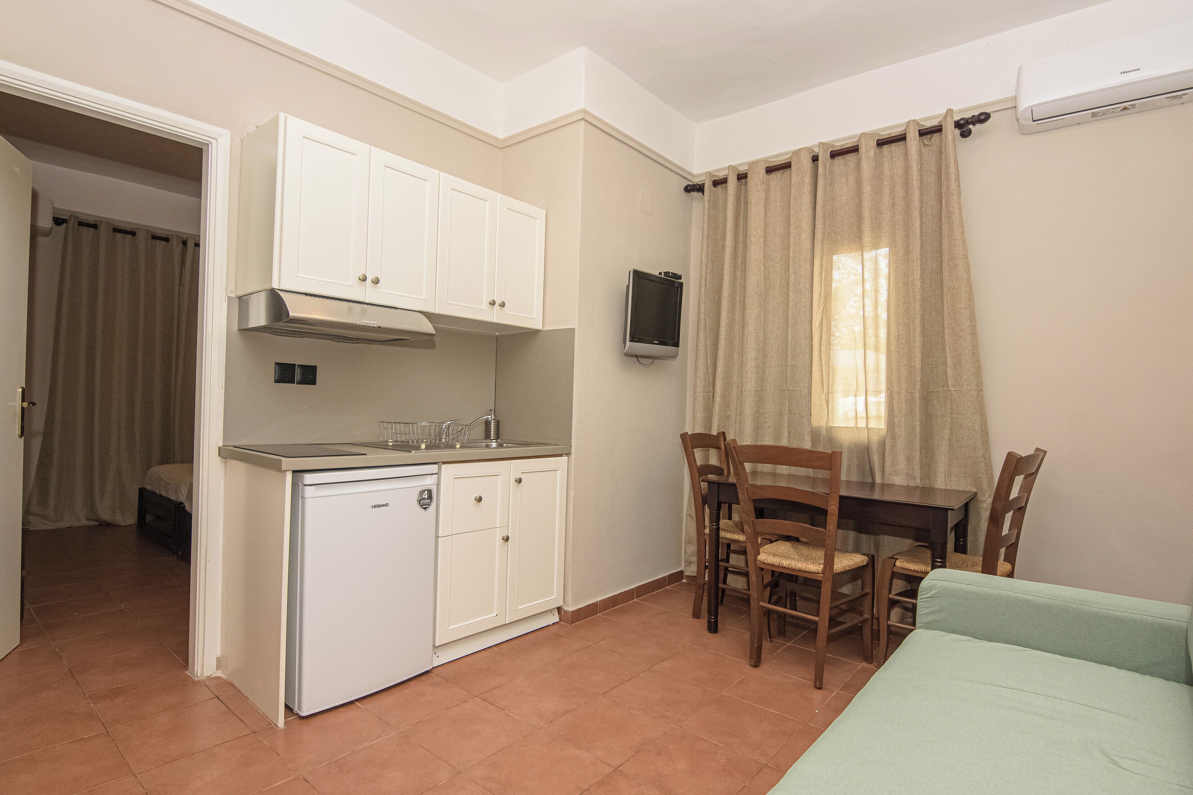 Une pièce compacte comprenant un coin cuisine, une table à manger avec des chaises, un téléviseur fixé au mur et un lit.
