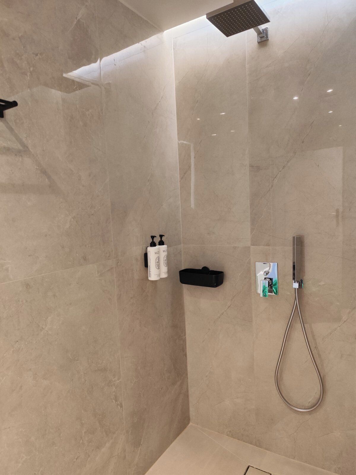 A modern bathroom with a glass-enclosed shower, marble walls, and a handheld showerhead.