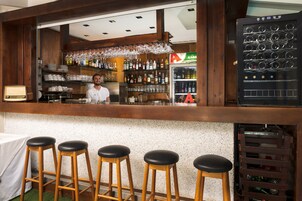 A bar area with stools, a refrigerator stocked with bottles, and shelves with glasses and bottles.
