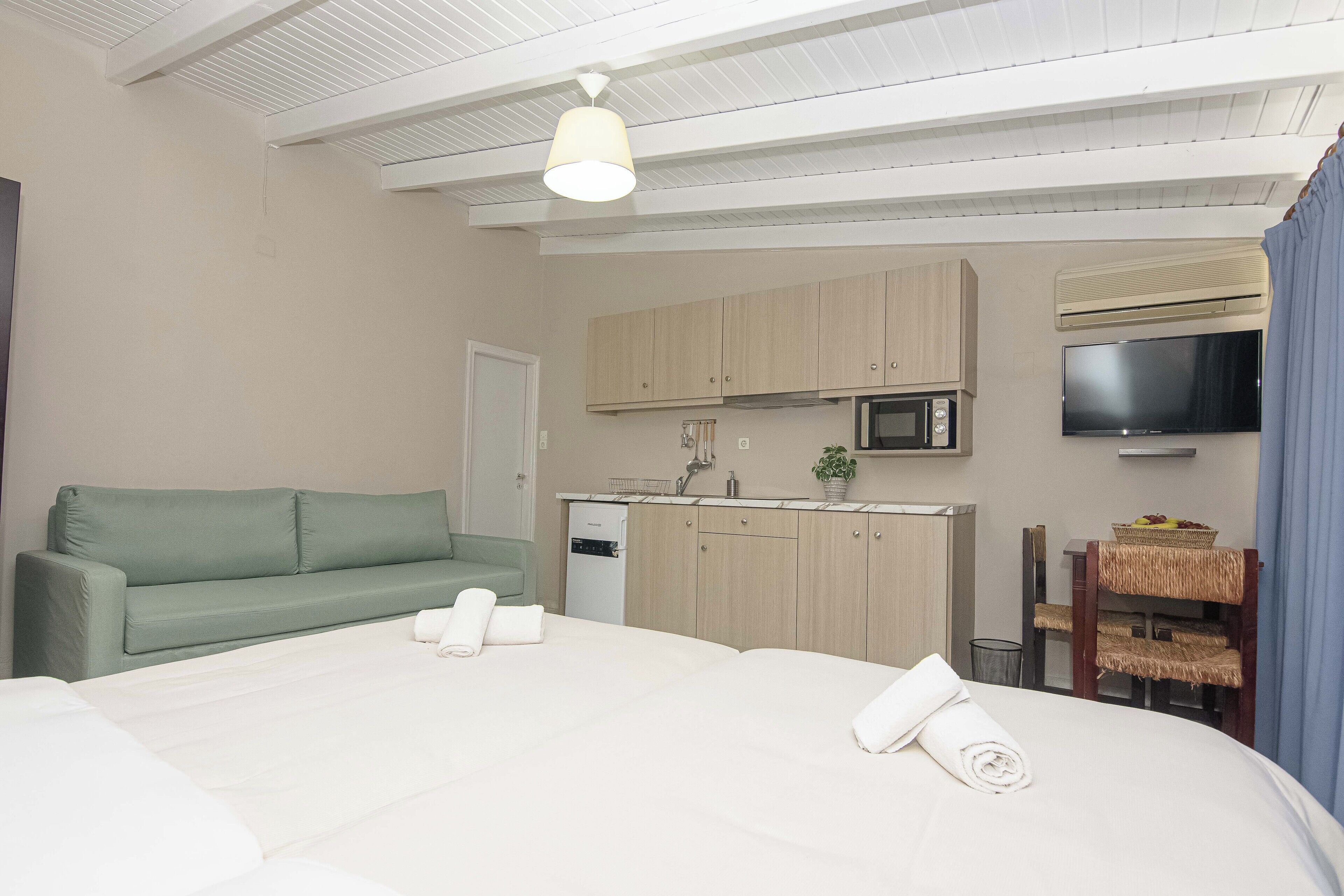 Een hotelkamer met een bed, een groene bank, een kitchenette met een magnetron en een televisie.