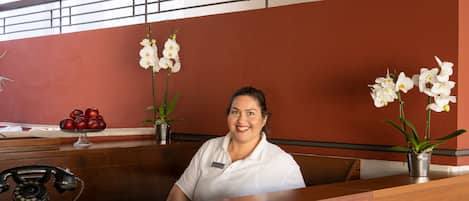 A reception desk with a telephone, a vase with red apples, and white orchids.