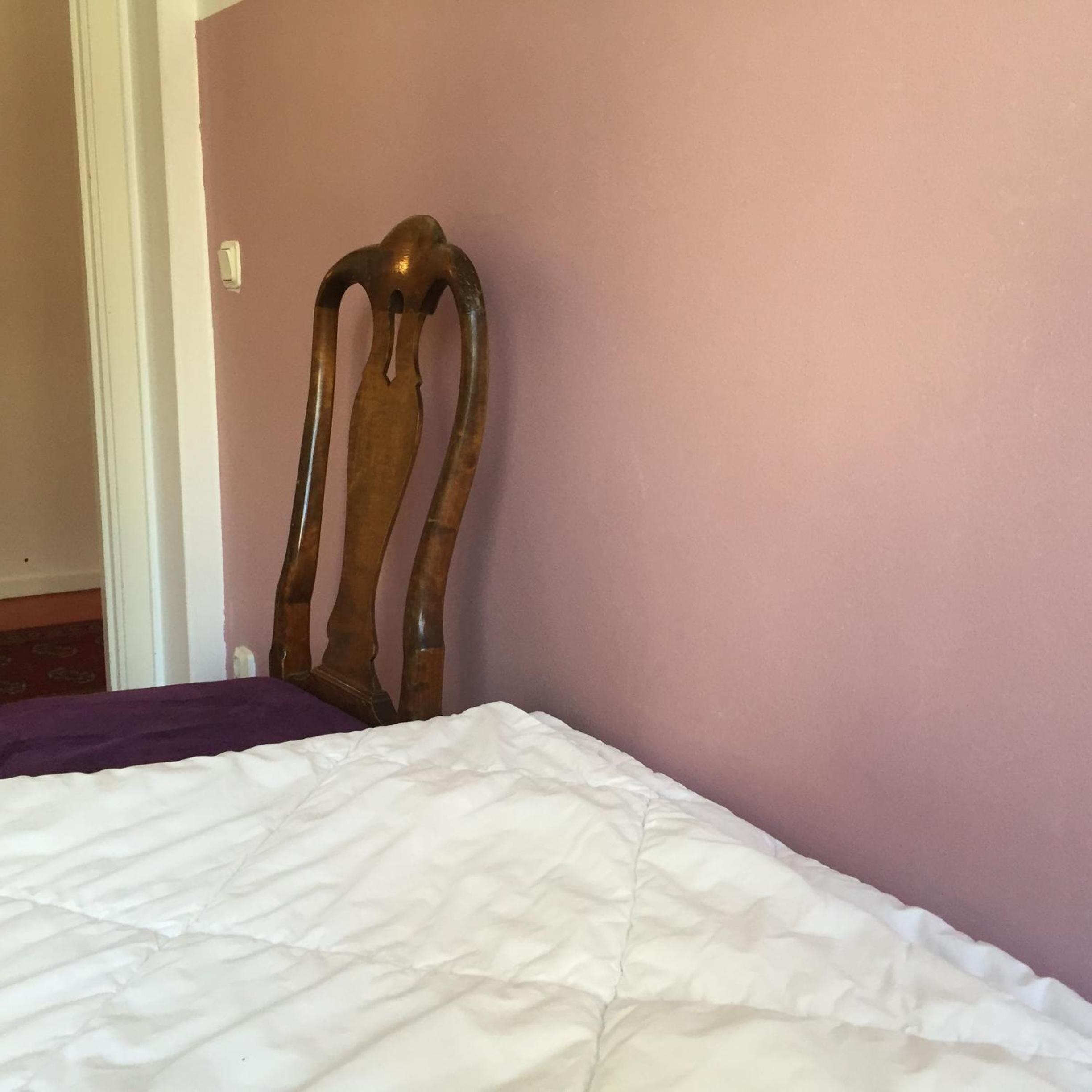 Una cama con edredón blanco en una habitación con cabecera de madera frente a una pared rosa.
