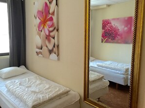 A hotel room with two single beds, a large mirror, and floral artwork on the walls. - Linne Hostel (Gothenburg)