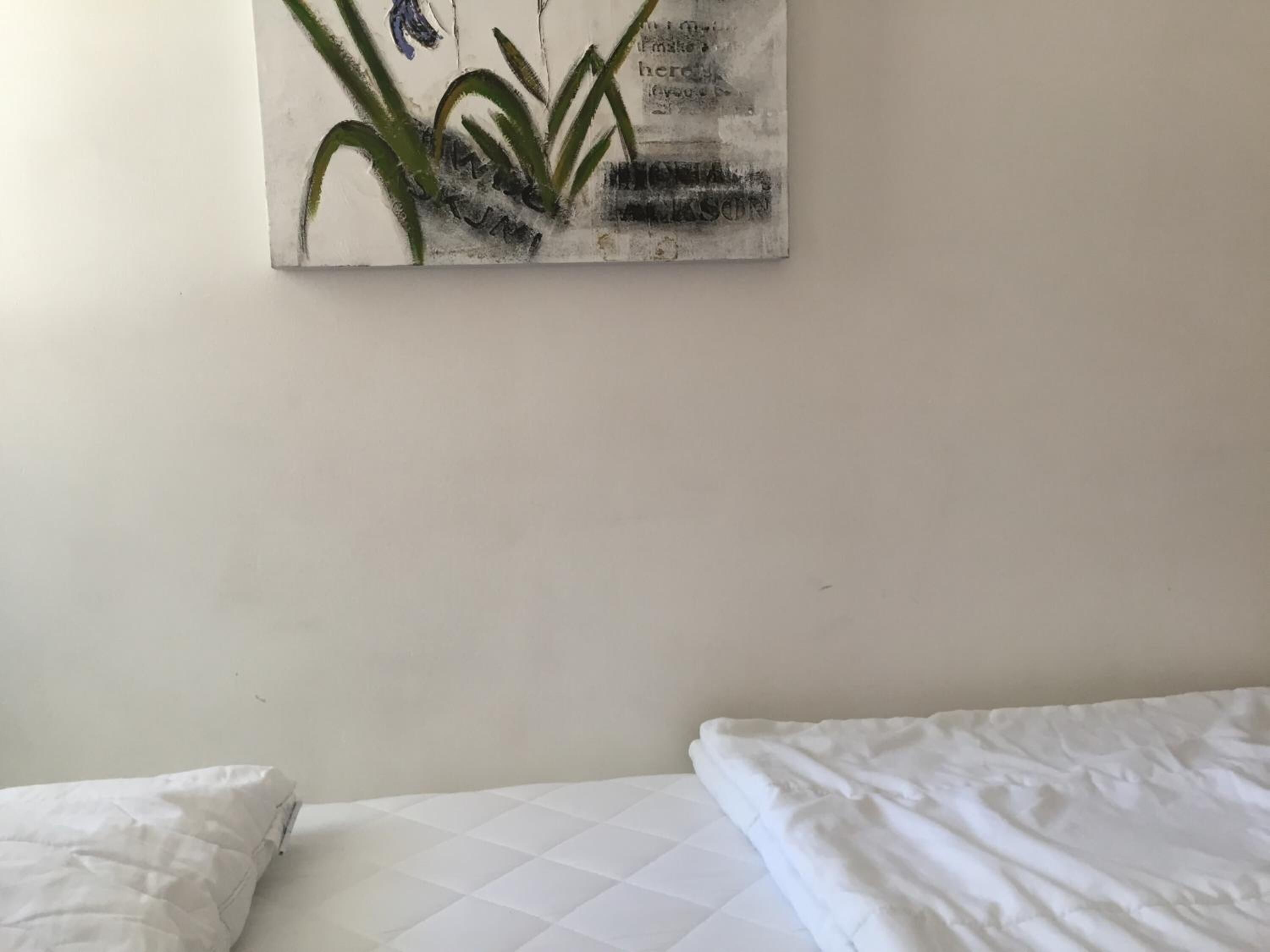 Un dormitorio con cama, ropa de cama blanca y un cuadro colgado en la pared con plantas.