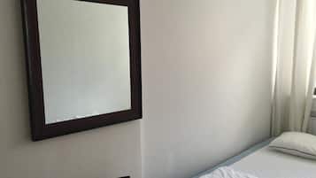 Una habitación sencilla con una cama, un espejo grande y una ventana con cortinas.