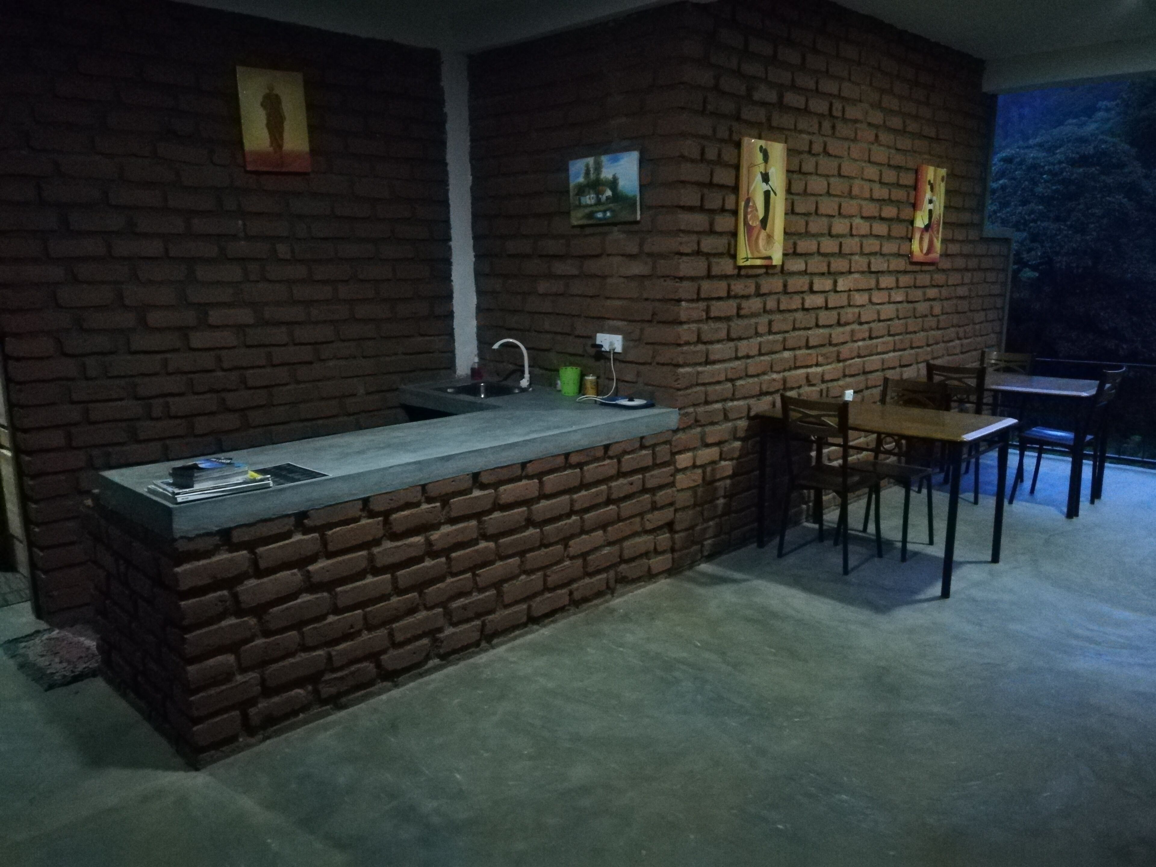 A kitchen area with a brick wall, a sink, and a counter. There are chairs and a table to the right.