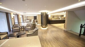 A modern hotel lobby with a seating area, a central decorative column, and a kitchen in the background. - Grand Laleli Hotel (Istanbul)
