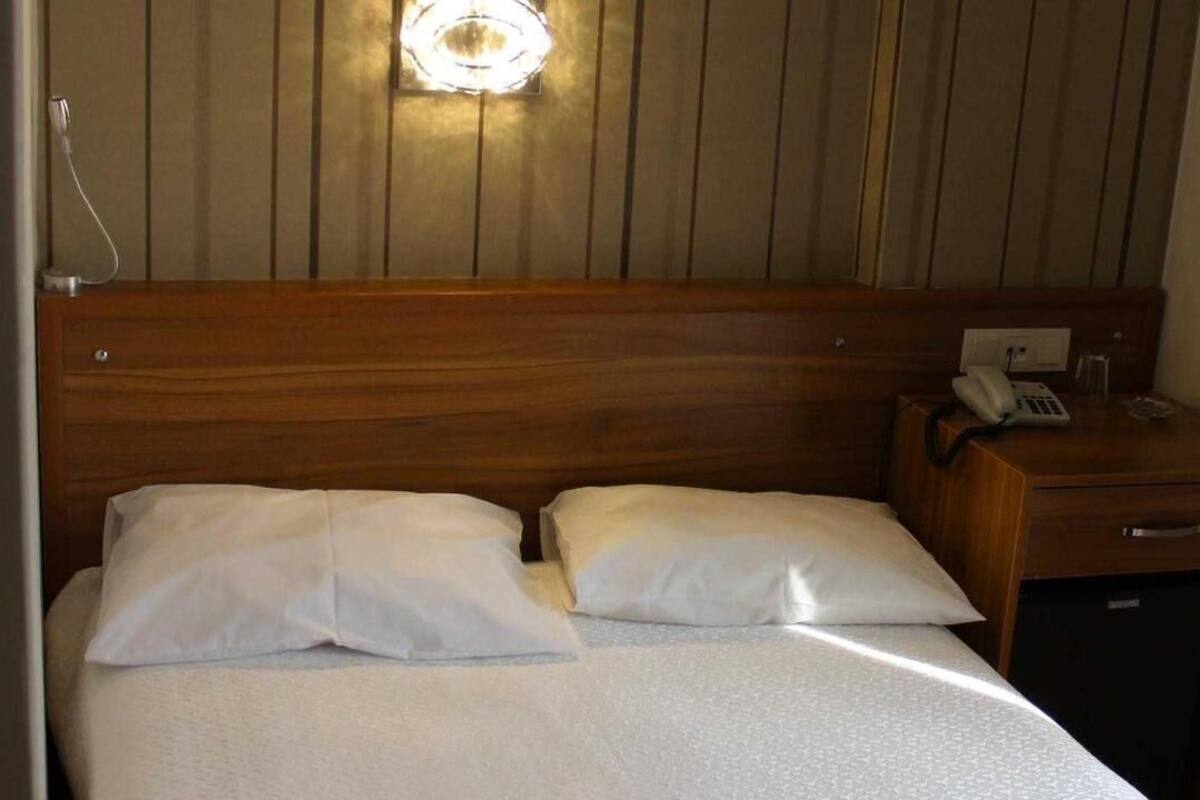 A hotel room with a wooden headboard, two white pillows, a bedside table with a telephone, and a small cabinet.