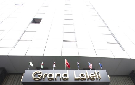 The Grand Laleh entrance with a geometric facade, a plaque, and flags.