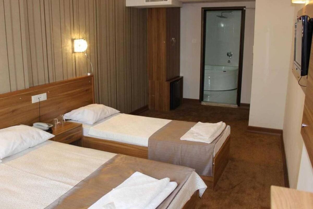 A hotel room with two beds, a wooden headboard, a small bedside table with a phone, and a glass shower door.