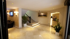 A modern hotel lobby with a marble floor, a staircase with a lighted handrail, a seating area, and a reception desk with a plant. - Grand Laleli Hotel (Istanbul)