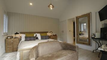 A bedroom with a bed, bedside tables, a sofa, a large mirror, and a TV.
