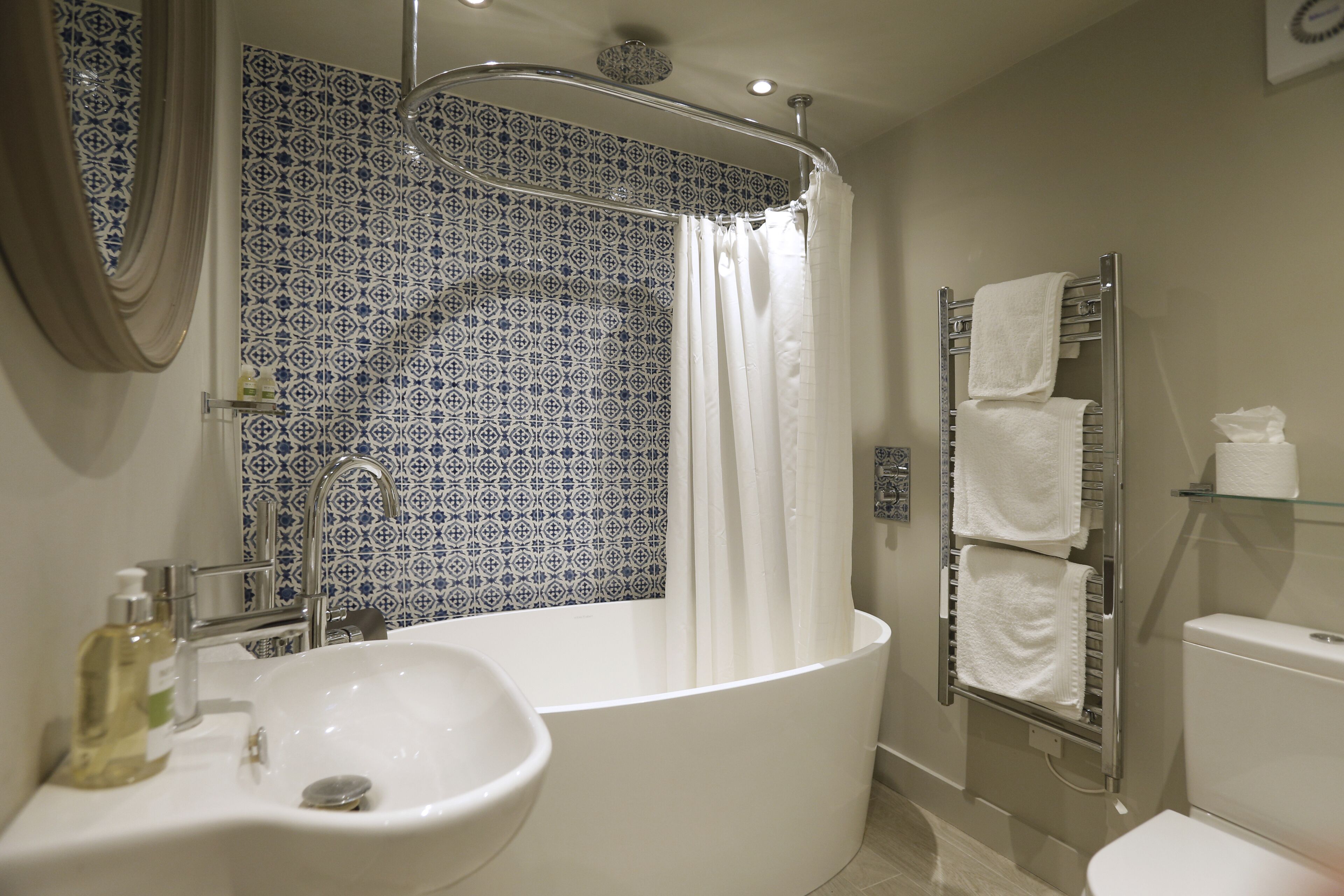 Un baño con una bañera independiente, un lavabo con espejo y un perchero con varias toallas.